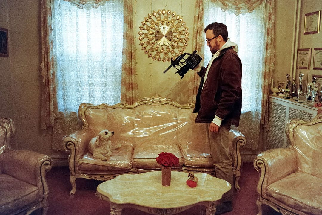 John Wilson holding his camera beside a dog on a plastic covered sofa