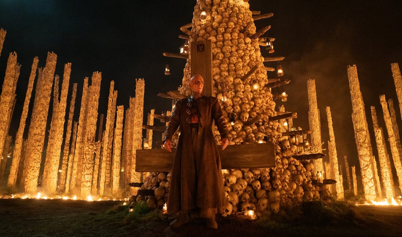 Ralph Fiennes as Dr Kelson beneath a tower of skulls in The Bone Temple